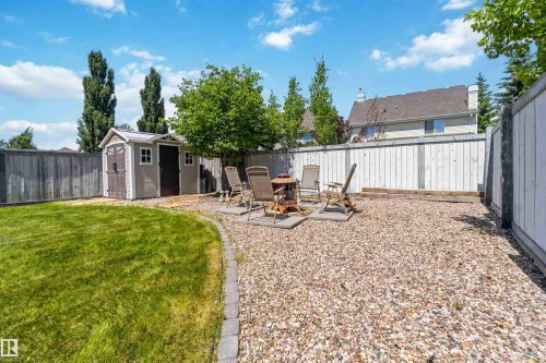 Spacious backyard featuring a dedicated gravel patio area with stone pavers, a manicured lawn, a storage shed, and mature trees - 3061 Spence Wynd, Edmonton, AB 