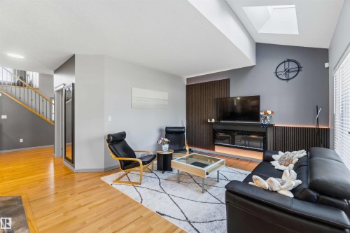 Living area featuring a vaulted ceiling with skylight, wood-finish flooring, a contemporary fireplace with accent lighting, and a dark wood-slat accent wall - 3061 Spence Wynd, Edmonton, AB 