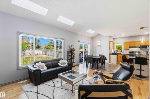 Open-concept living area featuring a vaulted ceiling with skylights, wood-finish flooring, a kitchen with wood cabinetry and stainless steel appliances, and a dining area with direct outdoor access - 3061 Spence Wynd, Edmonton, AB 