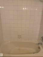 Alcove bathtub with white ceramic tile surround and chrome fixtures - 