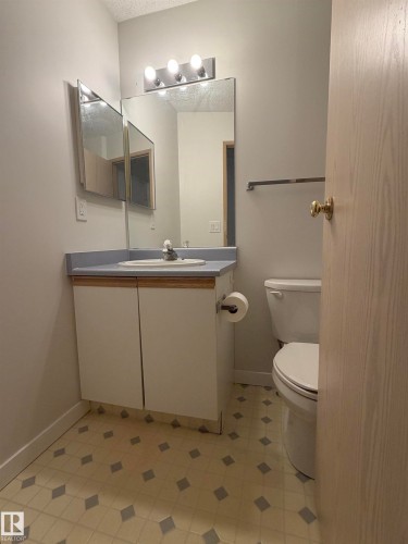 Bathroom featuring a vanity with an integrated sink, a large wall mirror, and overhead strip lighting - 213 17467 98A Avenue, Edmonton, AB 