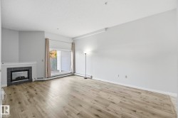 Spacious living area featuring wood-finish flooring, a corner fireplace with a dark tile surround, and direct access to an outdoor space through sliding glass doors - 