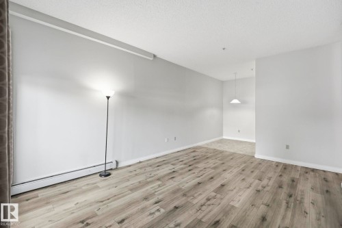 Spacious interior featuring wide plank wood-finish flooring, light gray wall paint, and white baseboards - 105 11446 40 Avenue Nw, Edmonton, AB 