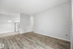 Spacious interior featuring wood-finish flooring, light-colored walls, and a recessed kitchen area with a white refrigerator and upper cabinetry - 