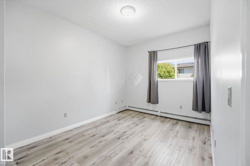 Bright room featuring wood-finish flooring, a window with exterior scenery, and white baseboards - 105 11446 40 Avenue Nw, Edmonton, AB 