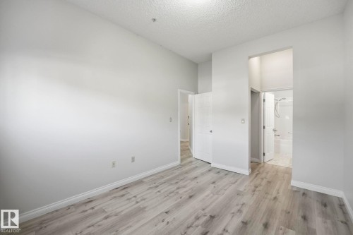 Spacious interior featuring wood-finish flooring, light grey wall tones, and white baseboards - 105 11446 40 Avenue Nw, Edmonton, AB 