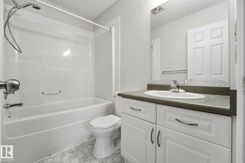 Bathroom featuring a white bathtub/shower combination, hexagon tile flooring, a single vanity with an integrated sink, a dark countertop, and paneled white cabinetry - 105 11446 40 Avenue Nw, Edmonton, AB 