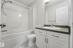 Bathroom featuring a white bathtub/shower combination, hexagon tile flooring, a single vanity with an integrated sink, a dark countertop, and paneled white cabinetry - 