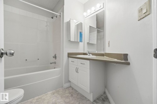 Bathroom featuring a white tub with shower, hexagonal floor tiling, a vanity with a white cabinet, and an integrated sink with a countertop - 105 11446 40 Avenue Nw, Edmonton, AB 