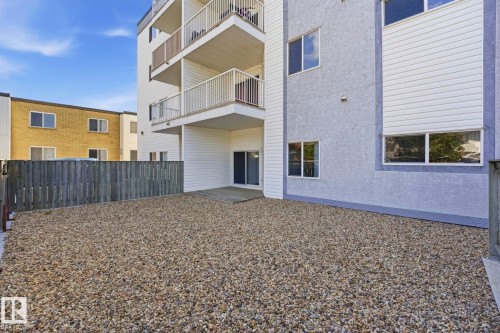 Gravel outdoor patio area featuring a wooden privacy fence, a ground-level deck, and sliding patio doors - 105 11446 40 Avenue Nw, Edmonton, AB 