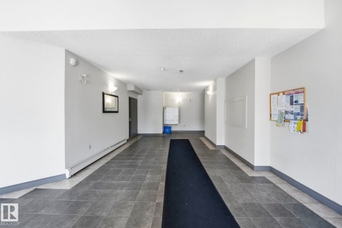 Main hallway featuring dark-toned tile flooring, light-toned walls, and sconce lighting - 105 11446 40 Avenue Nw, Edmonton, AB 