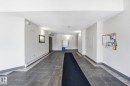 Main hallway featuring dark-toned tile flooring, light-toned walls, and sconce lighting - 105 11446 40 Avenue Nw, Edmonton, AB 