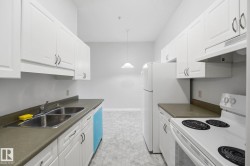 Galley kitchen featuring white cabinetry with dark hardware, a double basin stainless steel sink, a built-in dishwasher, and a white electric range with an overhead vent - 