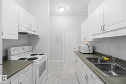Galley kitchen featuring white cabinetry with silver-tone hardware, dark countertops, hexagonal floor tiling, a double basin stainless steel sink, and a white range with overhead ventilation - 