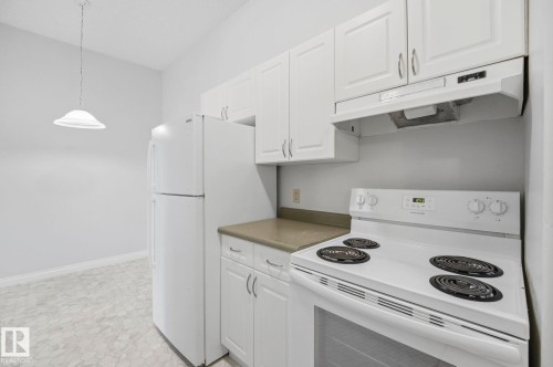 Kitchen featuring white cabinetry, solid surface countertops, white appliances, and patterned flooring - 105 11446 40 Avenue Nw, Edmonton, AB 