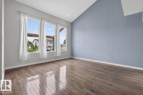 Vaulted ceiling room featuring a vertical plank accent wall, wood-finish flooring, and multiple windows with white trim - 2712 104 Street, Edmonton, AB 
