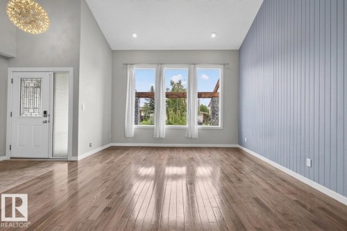 Spacious living area featuring polished wood-finish flooring, a contemporary accent wall with vertical paneling, and a prominent chandelier - 2712 104 Street, Edmonton, AB 
