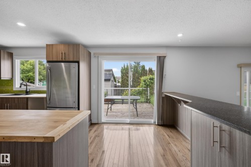 Open-concept kitchen with wood-finish flooring, two-tone cabinetry, stainless steel appliances, and a green tile backsplash - 2712 104 Street, Edmonton, AB 