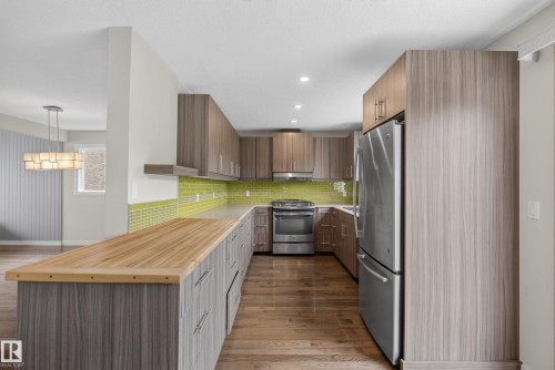 Kitchen featuring wood-finish flooring, stainless steel appliances, a vibrant green subway tile backsplash, recessed lighting, and a butcher block island countertop - 2712 104 Street, Edmonton, AB 