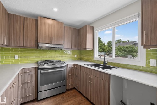 Contemporary kitchen featuring a stainless steel gas range, wood-grain cabinetry, light-toned countertops, a vibrant green subway tile backsplash, and a double basin sink with a matte black faucet - 2712 104 Street, Edmonton, AB 