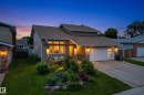 Contemporary residence featuring a two-car garage with frosted glass panels, stone column accents, a landscaped front yard with varied plantings, and a concrete driveway - 2712 104 Street, Edmonton, AB 