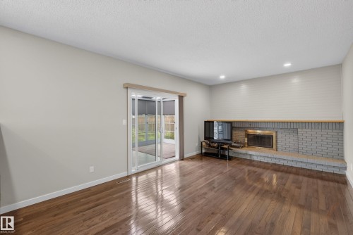 Spacious room featuring wood-finish flooring, a brick fireplace surround with a brass insert, and a wood mantel - 2712 104 Street, Edmonton, AB 