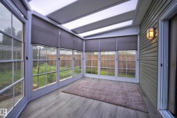 Enclosed sunroom featuring a ceiling with integrated lighting, multiple windows with grid patterns, roller shades, and wood-finish flooring - 