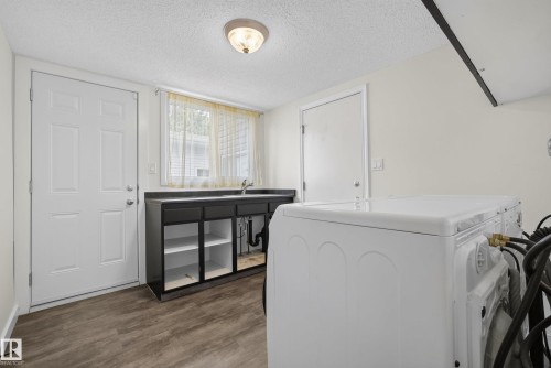 Laundry area featuring wood-finish flooring, a utility sink with dark cabinetry, and two white paneled doors - 2712 104 Street, Edmonton, AB 