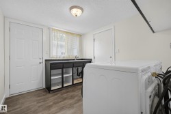 Laundry area featuring wood-finish flooring, a utility sink with dark cabinetry, and two white paneled doors - 