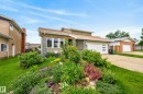 Modern split-level residence featuring a multi-pane garage door, stone and siding exterior, and a sloped front yard with established landscaping and various plantings - 2712 104 Street, Edmonton, AB 