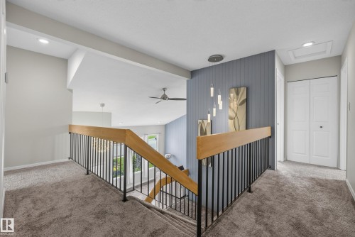 Carpeted landing featuring a wooden handrail with black metal balusters, recessed lighting, a modern ceiling fan, and a paneled accent wall with a contemporary pendant fixture - 2712 104 Street, Edmonton, AB 