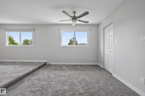 Spacious room featuring neutral carpeting, light gray walls, a ceiling fan with integrated lighting, two windows with white trim, and a bi-fold closet door - 2712 104 Street, Edmonton, AB 