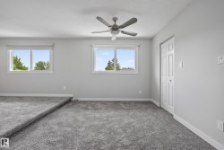 Spacious room featuring neutral carpeting, light gray walls, a ceiling fan with integrated lighting, two windows with white trim, and a bi-fold closet door - 