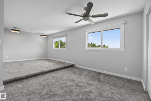 Spacious carpeted room featuring a ceiling fan, two windows, two flush-mount ceiling lights, and an elevated section - 2712 104 Street, Edmonton, AB 