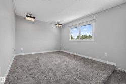 Spacious room featuring light gray walls, gray carpeting, a large window, and two ceiling-mounted light fixtures - 
