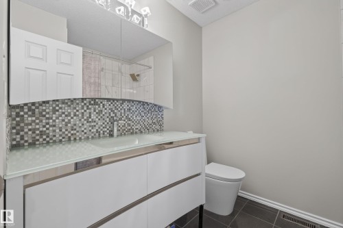 Bathroom vanity featuring a frosted glass countertop, contemporary white cabinetry, and a mosaic tile backsplash - 2712 104 Street, Edmonton, AB 