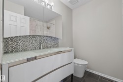 Bathroom vanity featuring a frosted glass countertop, contemporary white cabinetry, and a mosaic tile backsplash - 