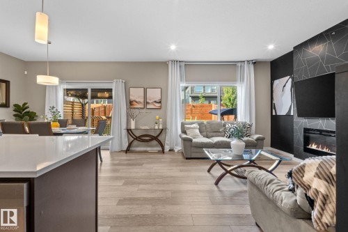 Expansive open-concept living area featuring wood-finish flooring, a modern black accent wall with geometric detailing, a built-in linear fireplace, and recessed lighting - 2146 Koshal Way, Edmonton, AB 