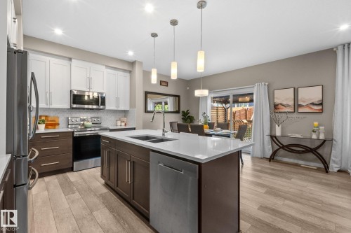 Contemporary kitchen featuring an island with a double sink, stainless steel appliances, and two-tone cabinetry - 2146 Koshal Way, Edmonton, AB 