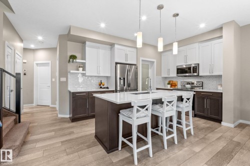 Modern kitchen featuring a central island with countertop seating, stainless steel appliances, two-tone cabinetry, and wood-finish flooring - 2146 Koshal Way, Edmonton, AB 