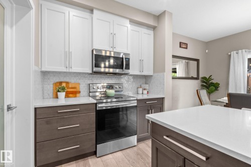 Modern kitchen featuring white upper cabinetry, dark wood-finish lower cabinetry, and stainless steel appliances - 2146 Koshal Way, Edmonton, AB 