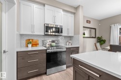 Modern kitchen featuring white upper cabinetry, dark wood-finish lower cabinetry, and stainless steel appliances - 