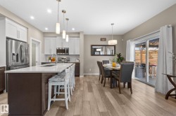 Open-concept kitchen and dining area featuring light wood-finish flooring, a kitchen island with seating, stainless steel appliances, white upper cabinetry, and a sliding glass door - 