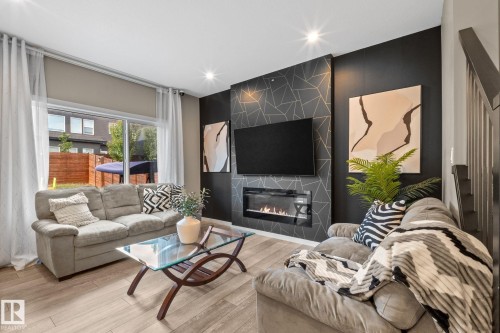 Living area featuring a modern fireplace with geometric accent wall, recessed lighting, wood-finish flooring, and a large sliding glass door - 2146 Koshal Way, Edmonton, AB 