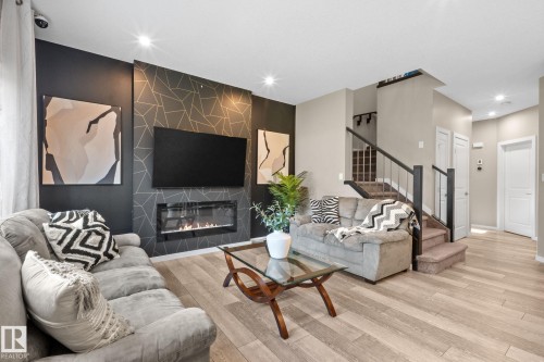 Living space featuring a striking accent wall with geometric patterning, a built-in linear fireplace, recessed lighting, and wood-finish flooring - 2146 Koshal Way, Edmonton, AB 
