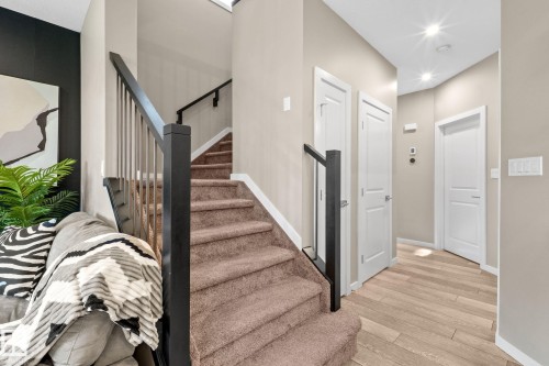 Staircase featuring dark wood newel posts and railings with vertical metal balusters, carpeted treads, and light neutral wall paint - 2146 Koshal Way, Edmonton, AB 