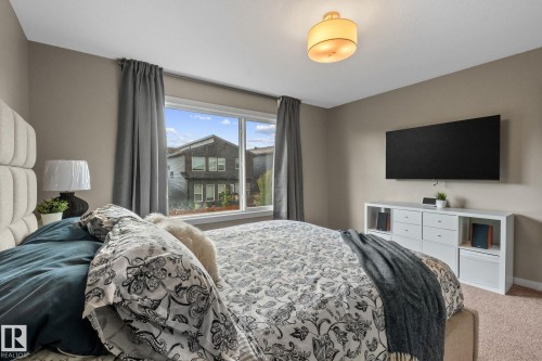 Bedroom featuring a large window with gray drapes, beige walls, and light-toned carpet - 2146 Koshal Way, Edmonton, AB 