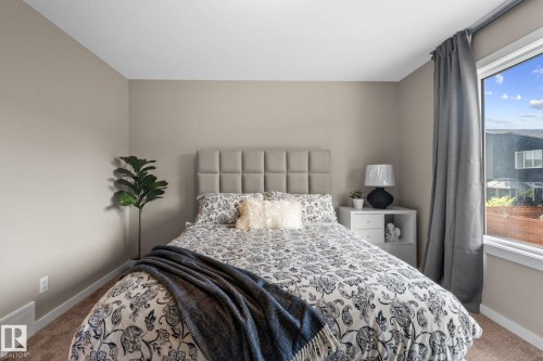 Bright bedroom featuring a large window, plush carpet flooring, a paneled headboard, and neutral wall tones - 2146 Koshal Way, Edmonton, AB 