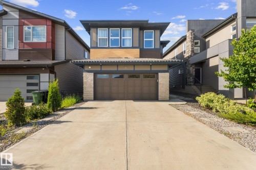 Modern two-story residence featuring a brown garage door, stone accents on the facade, and multiple upper-level windows - 2146 Koshal Way, Edmonton, AB 