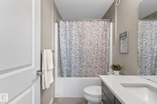 Bathroom featuring a built-in tub with a tile surround, a toilet, and a vanity with an integrated sink and countertop - 2146 Koshal Way, Edmonton, AB 